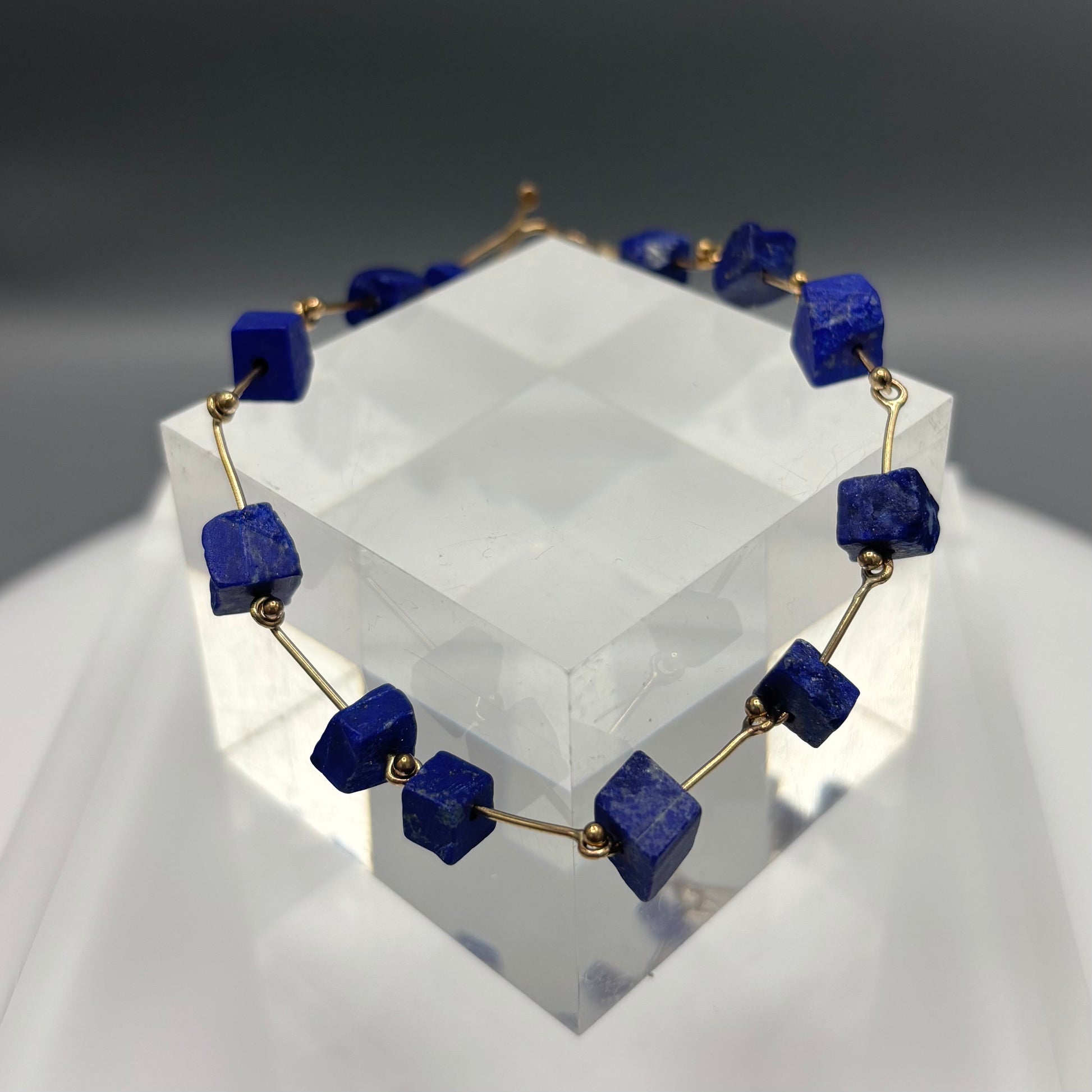 Necklace with blue square beads on a clear stand against a gray background