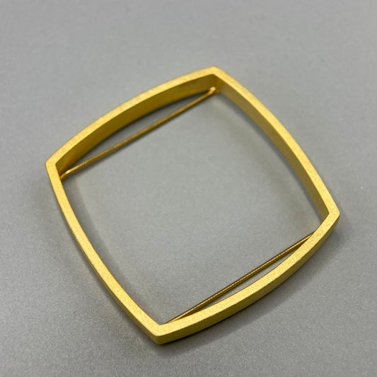 A square-shaped gold brooch with a smooth, yellow gold finish on a grey background.